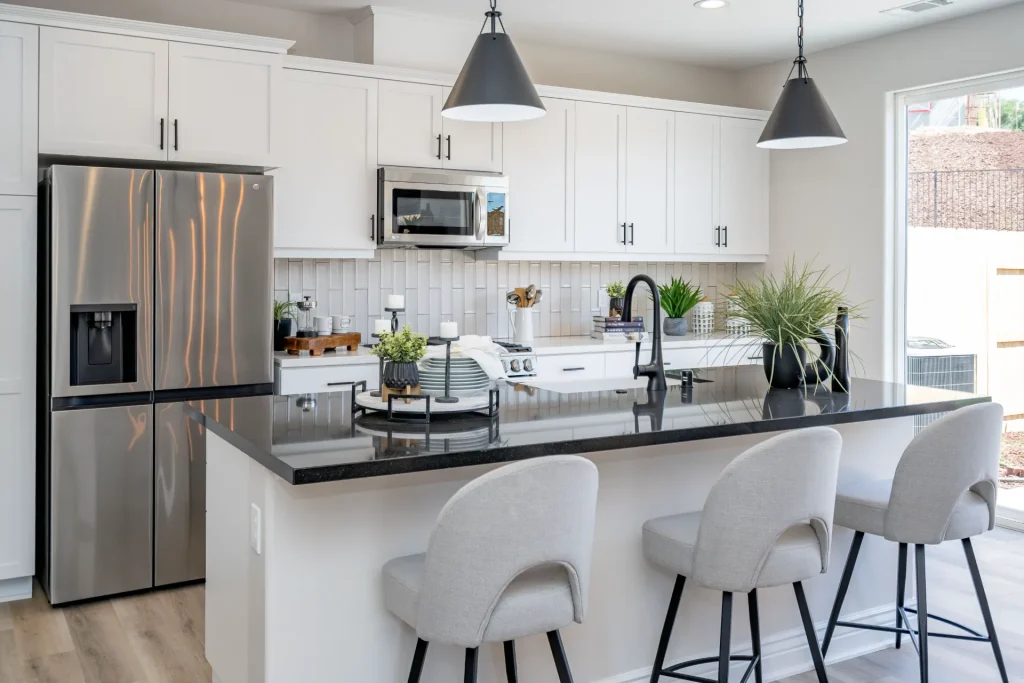 A white kitchen with black counter tops and stainless steel appliances, a Duet home